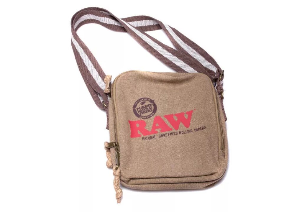 Brązowa torba na ramię marki RAW z przewiewnym paskiem. Torba jest ozdobiona wyraźnym czerwonym logo RAW i hasłem 'Natural Unrefined Rolling Papers', co podkreśla naturalny charakter produktów marki
